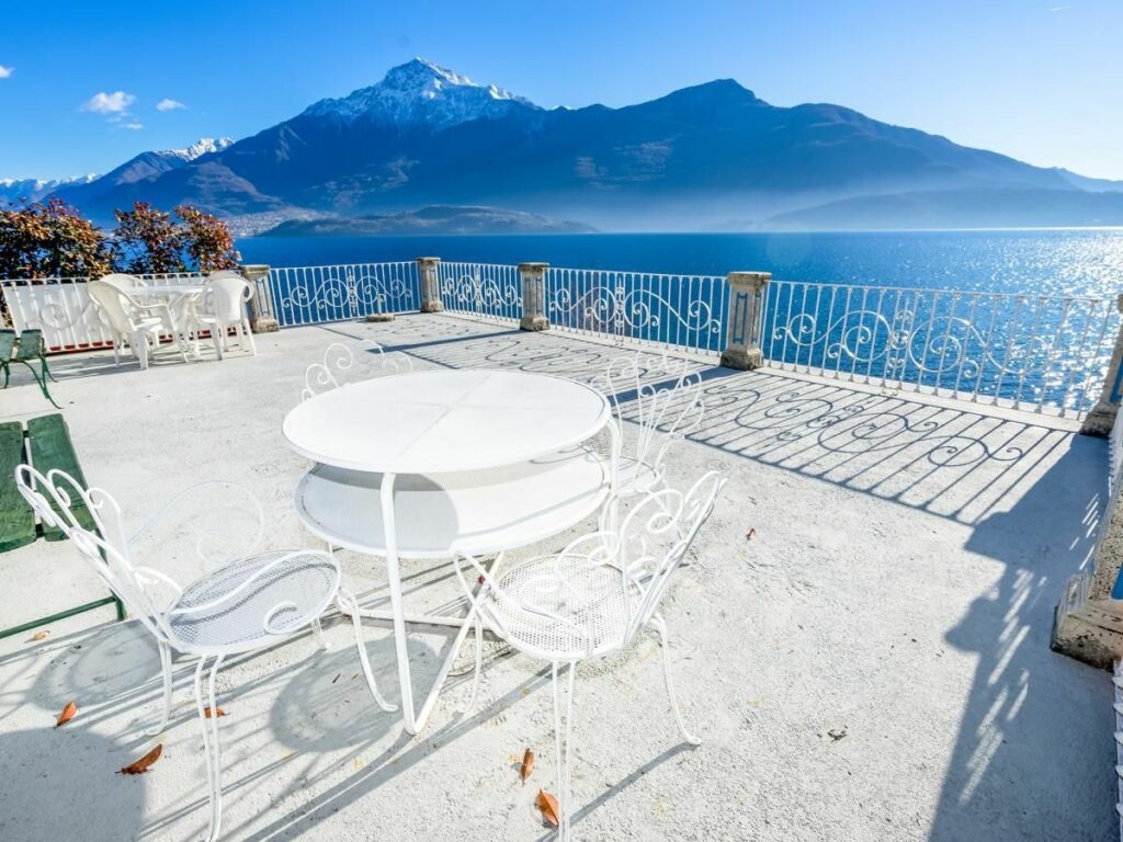 Kleiner weißer Tisch mit Stühlen vor einem atemberaubenden Ausblick auf den Comer See und die Berge