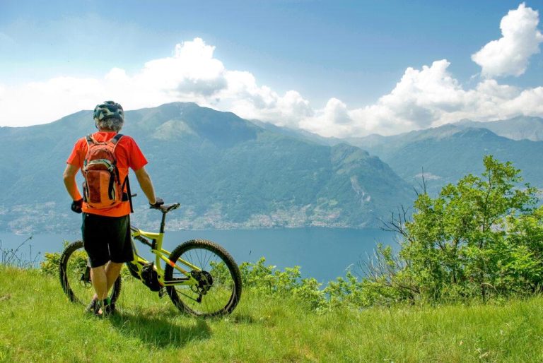 man with electric bicycle, e-bike, ebike, high mountains, observes horizon, valley and lake of Como, forest, summer, sport, adventure, cloud, alps, Italy
